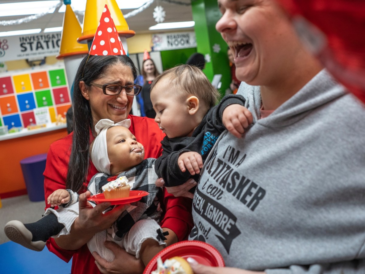 Flint pediatrician Dr. Mona Hanna with babies. She is wearing a birthday hat.