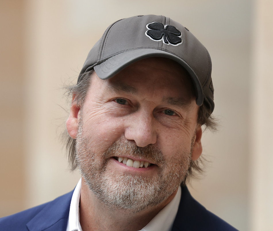 Headshot of a smiling bearded man wearing a baseball-style cap with a four-leaf clover on it.