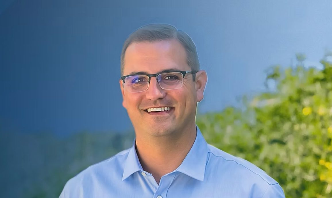 headshot of a man smiling with green and blue backdrop