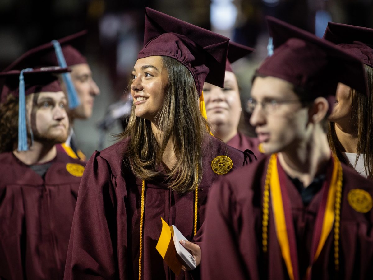 A young woman in cap and gown surrounded by a group of fellow college graduates.