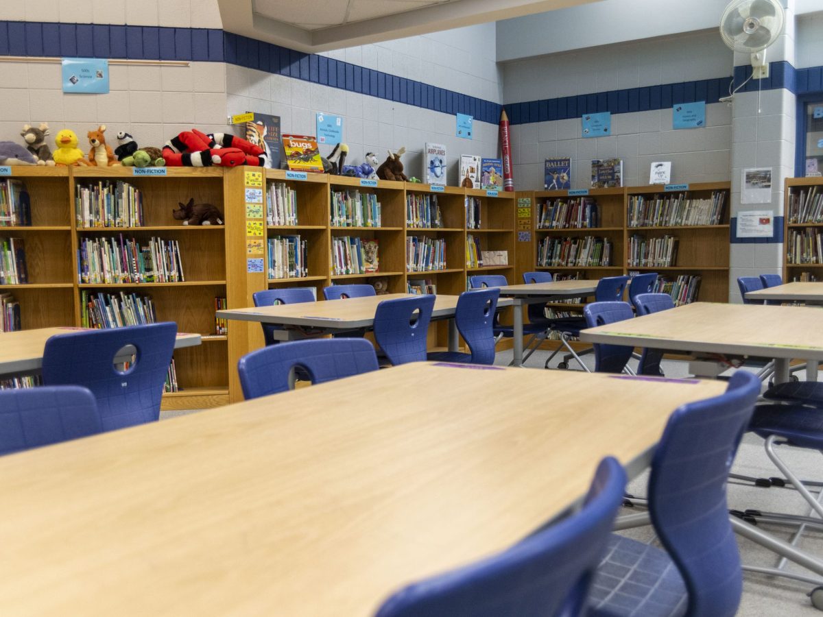 An empty library with blue chairs and long desks, lined by bookshelves