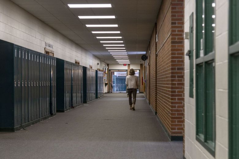 A teacher walks in a hallway. Lockers are on the side of the hallway. 