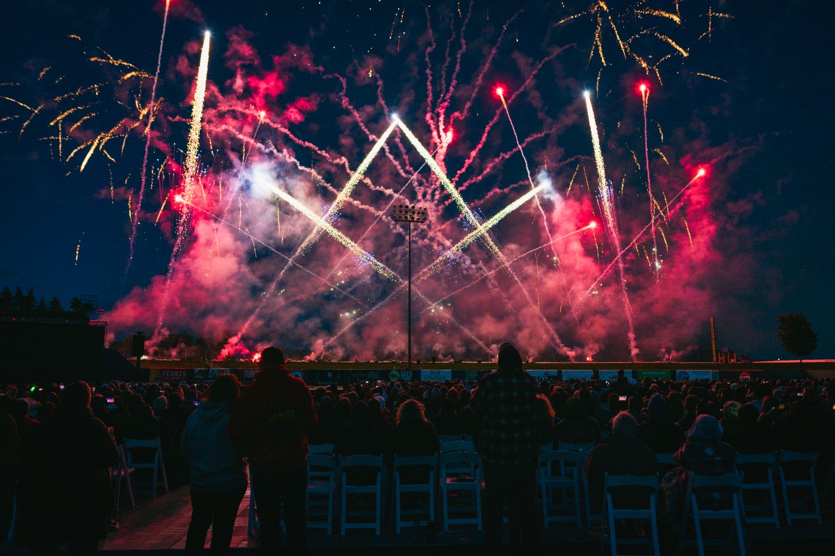A crowd sits in chairs to watch a fireworks display