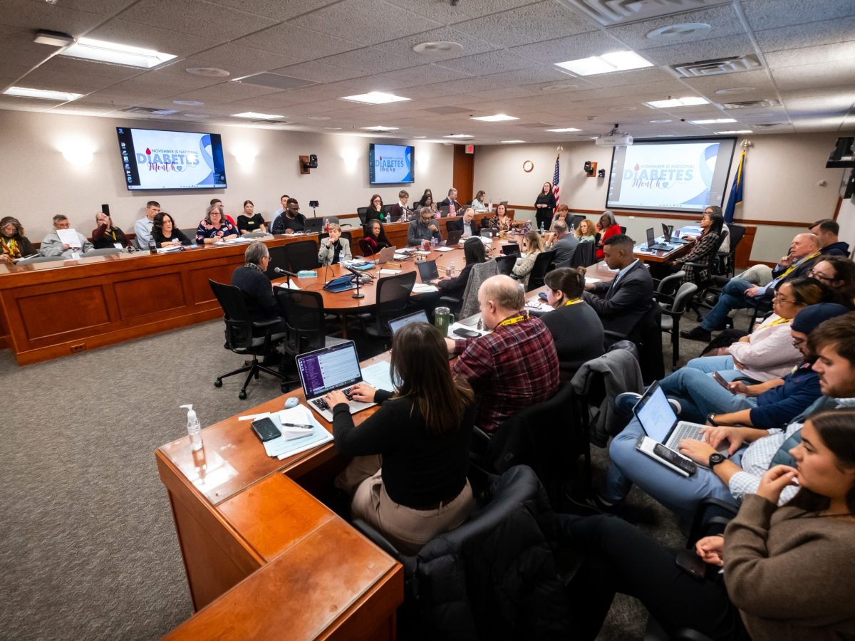 A crowded meeting room with reporters, board members and staff members of the Michigan Department of Education
