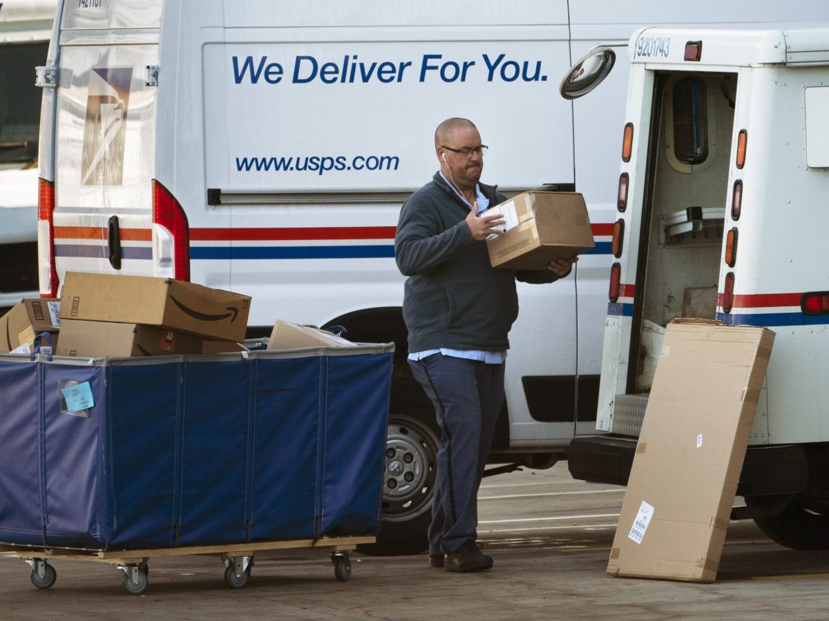 A postal carrier loads boxes into his delivery vehicle.