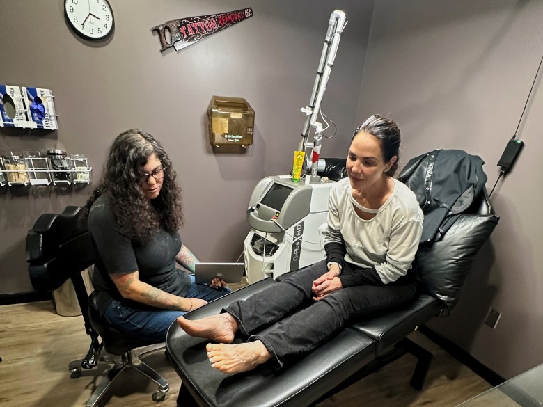 A woman sits up on an exam table while a person works at her side