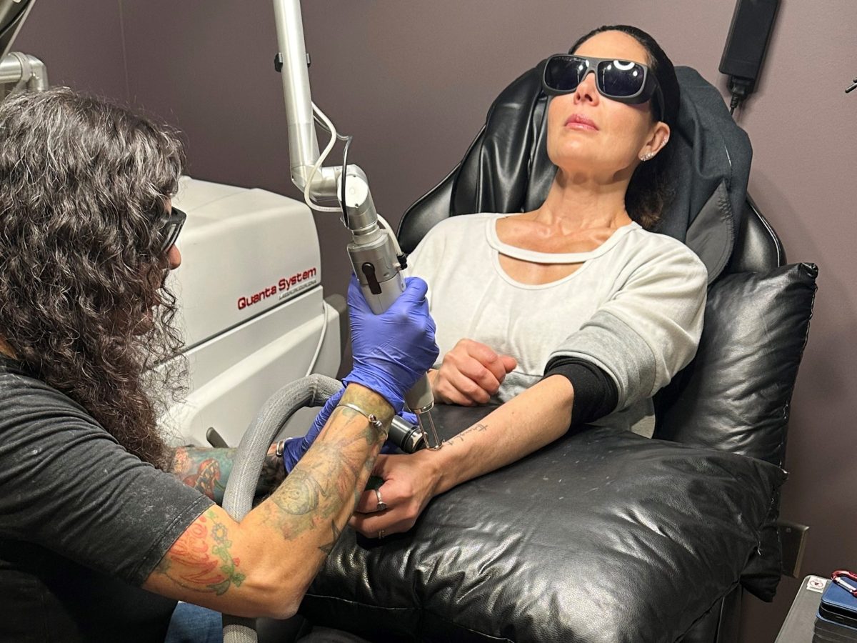 A woman wears goggles as a worker uses a laser to remove a tattoo from her arm