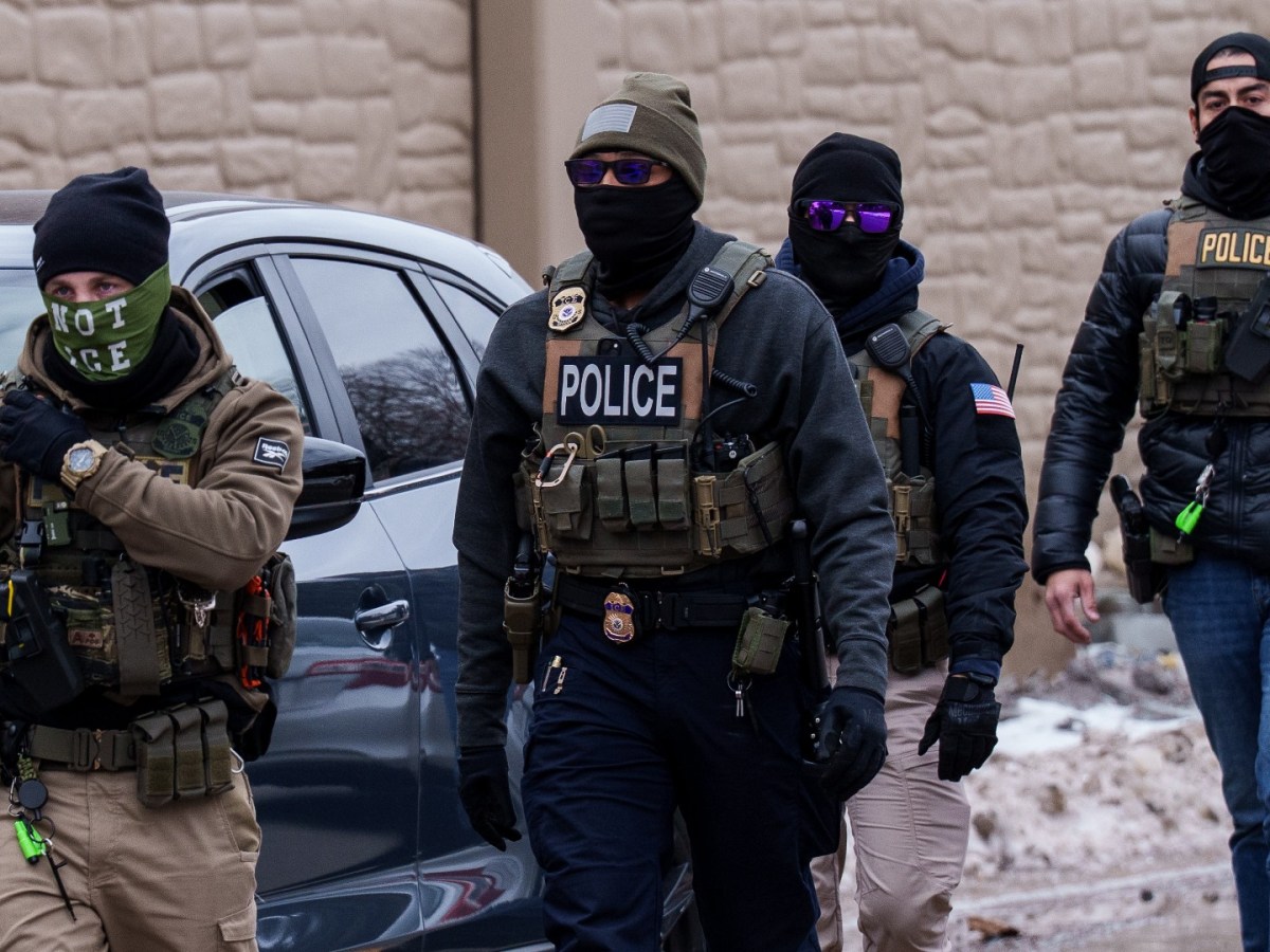ICE agents walk down the street in tactical gear and masks