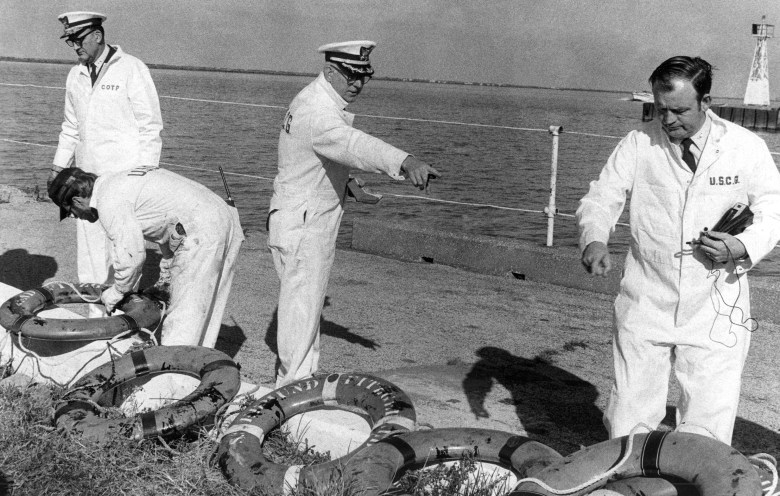 A black-and-white photo of four Coast Guard officers inspecting life rings. 