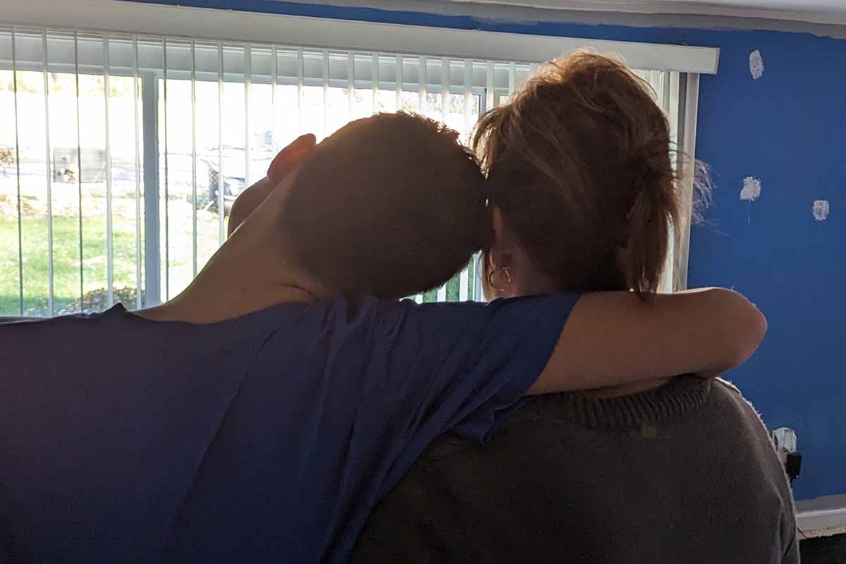 two people seen from behind in partial shadow looking out a window