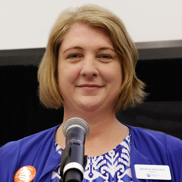 A woman smiling while standing or sitting in front of a microphone.