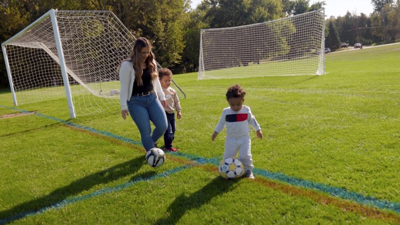A woman plays soccer with two children