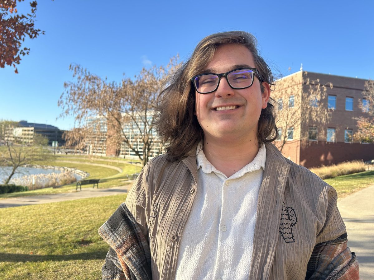 A male student stands outside with an academic building in the background