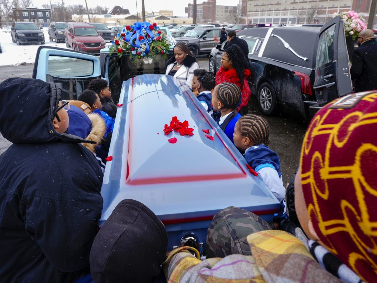 Many people are carrying a casket and putting it in a hearse.