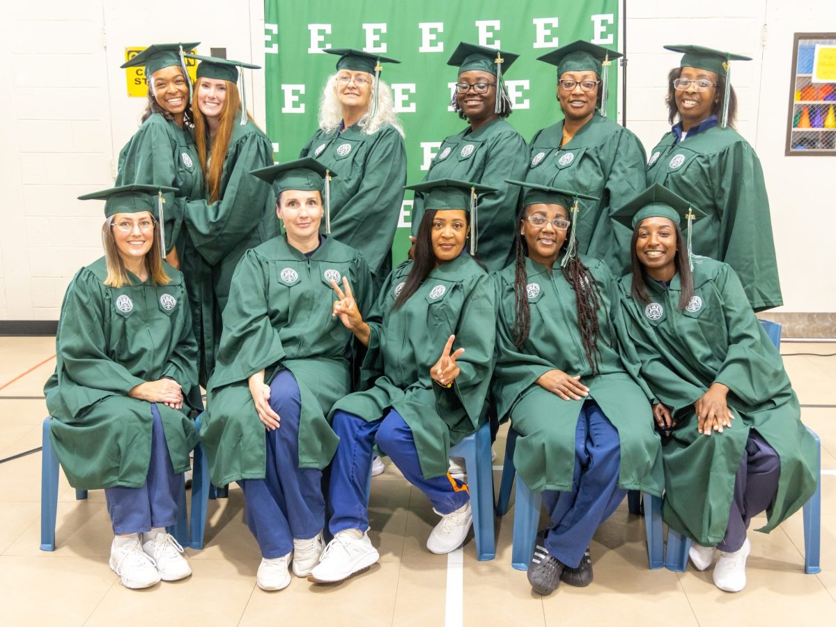 A group of women wearing graduation caps and gowns pose in front of an Eastern Michigan University backdrop