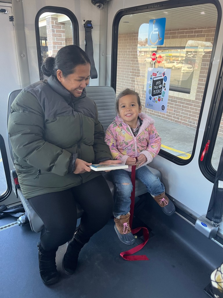 A woman and a child on a bus smiling as they look over a book.