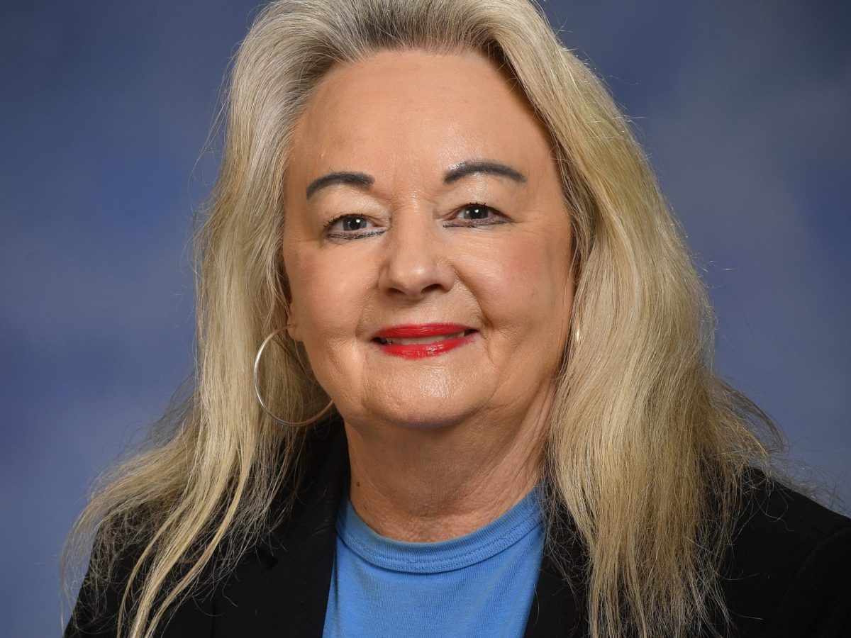 Headshot of a smiling woman wearing against a blue background