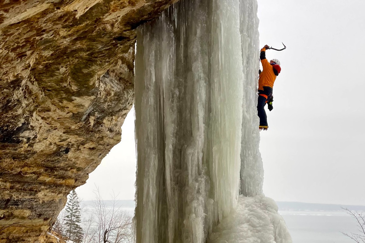 A man climbs a thick sheet of ice that's cascading down a rock face