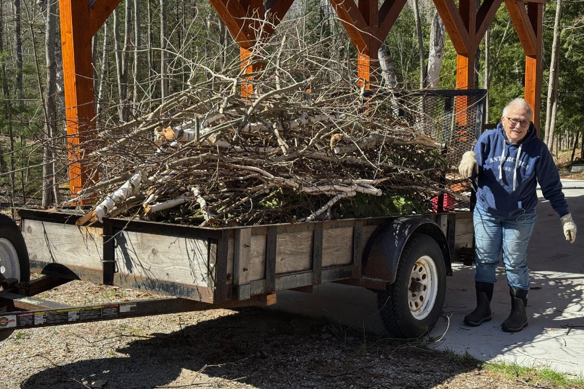 A woman stands next to a trailer full of tree limbs