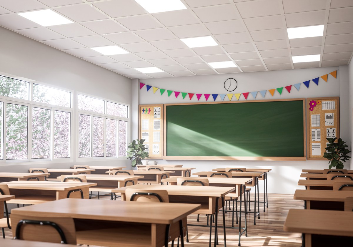 The classroom have white walls and wooden floor, decorated with wooden tables and chairs, large windows overlooking natural views.