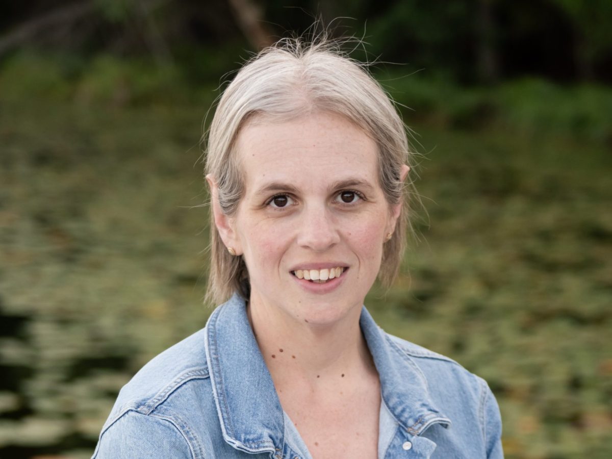 Headshot of a smiling woman with greenery in the background