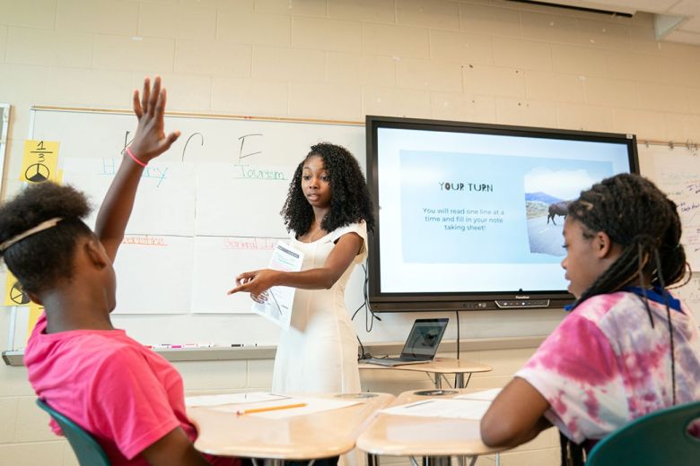A teacher points to a student with their hand up.