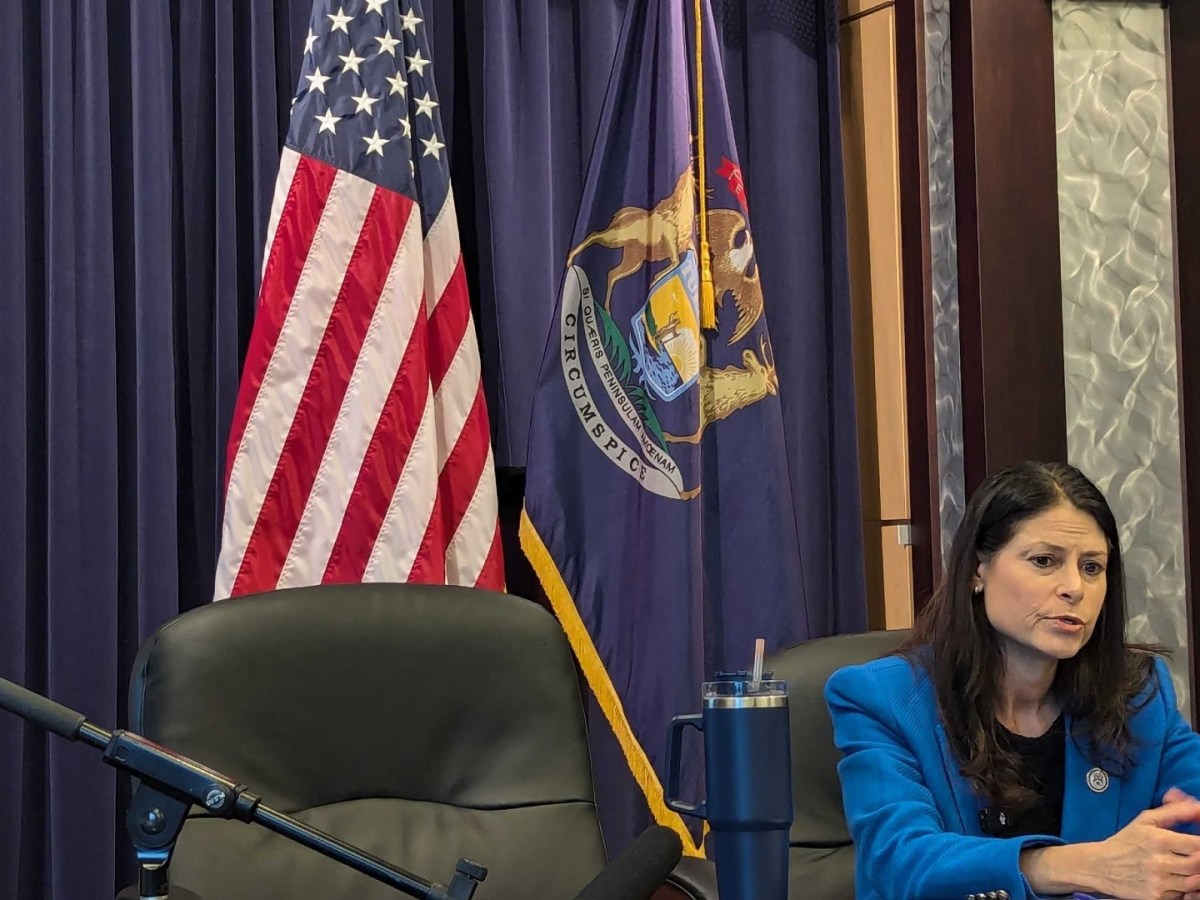 Dana Nessel sits at a table in front of the American flag and the Michigan flag
