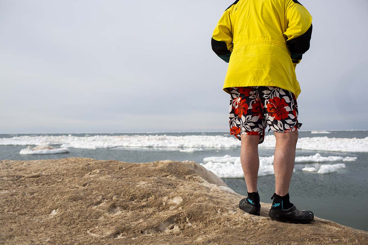 A man in a yellow shirt and shorts. He is about to jump in icy water.