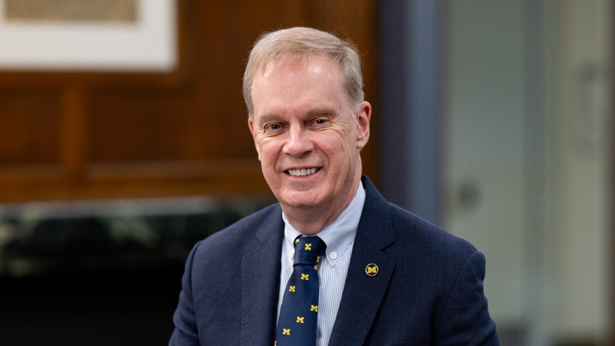 head and shoulders shot of a man in an office setting wearing a University of Michigan tie