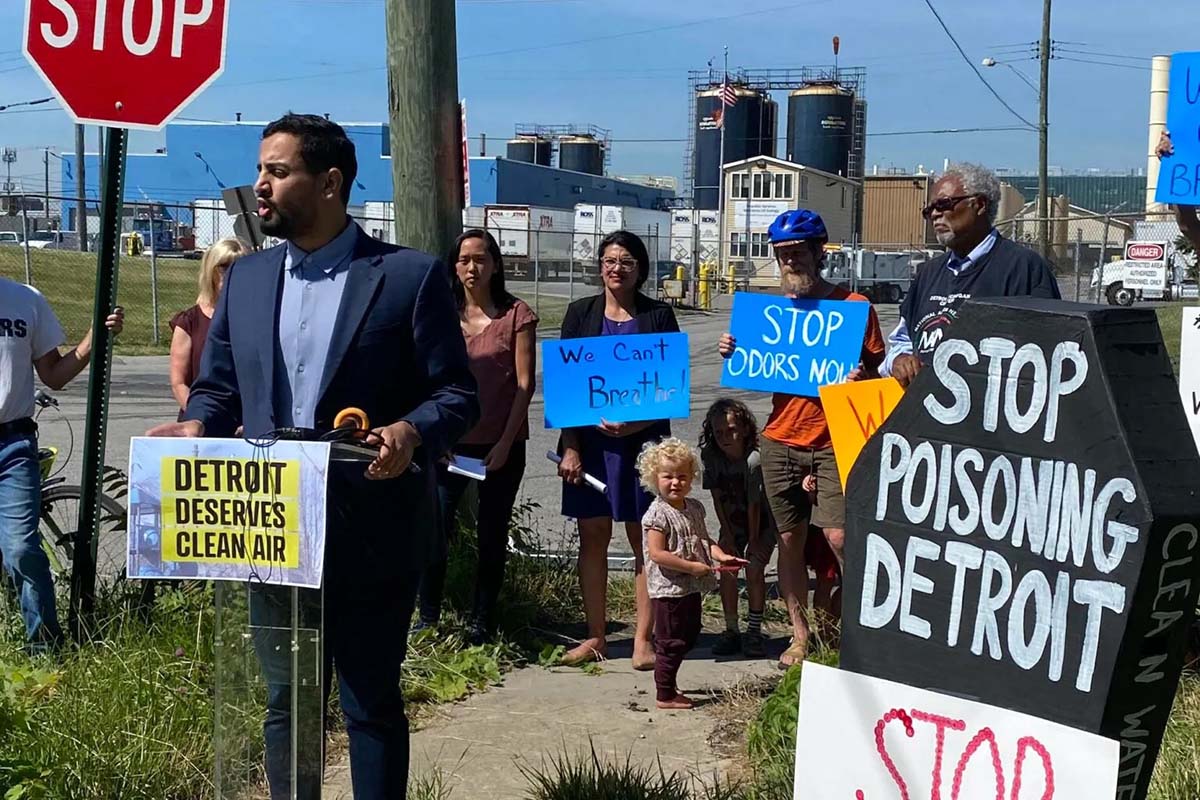 State Rep. Abraham Aiyash (D-Hamtramck) speaks at a protest at the US Ecology hazardous waste facility in Detroit. People are standing behind. They are on a street corner