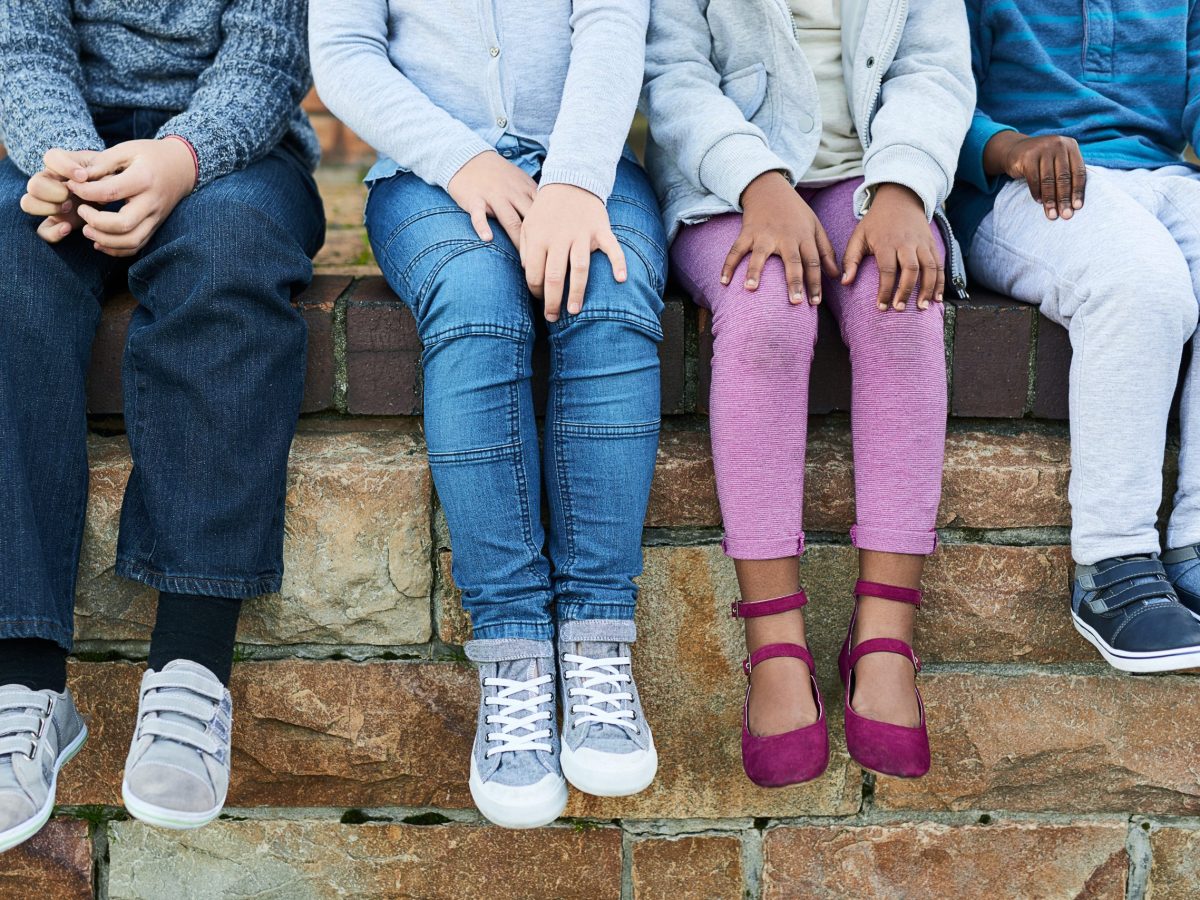 Shot of the legs and sneakers of four children seated side by side.