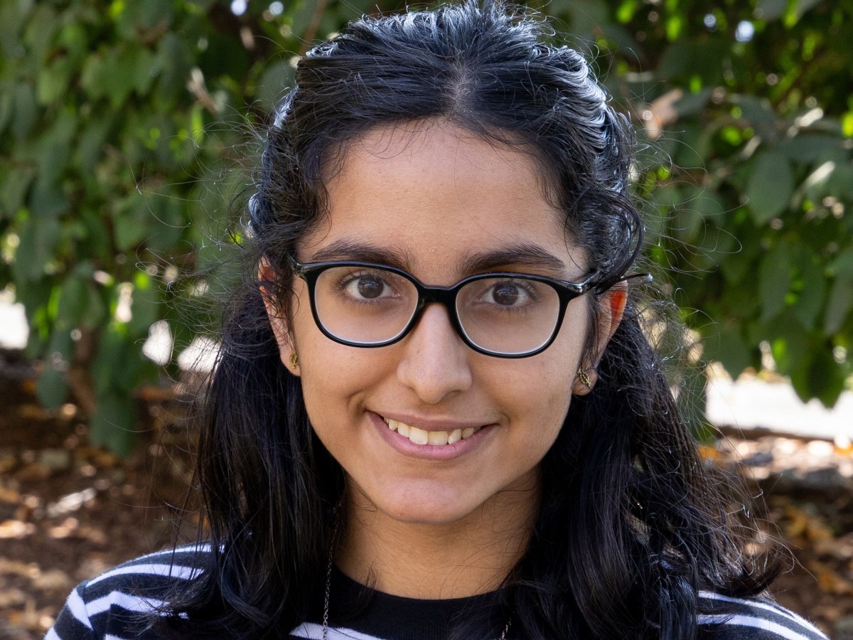 Headshot of an adolescent girl smiling with greenery in the background.