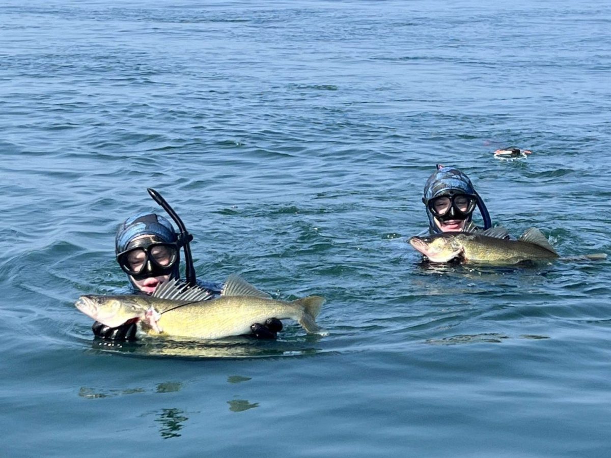 Two people in diving gear pose with fish in the water