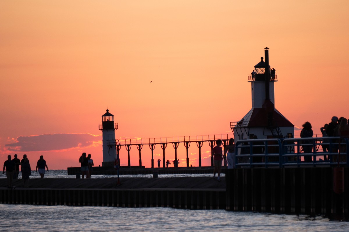 Silohuettes of people walking on a pier are seen with an orange sunset behind them