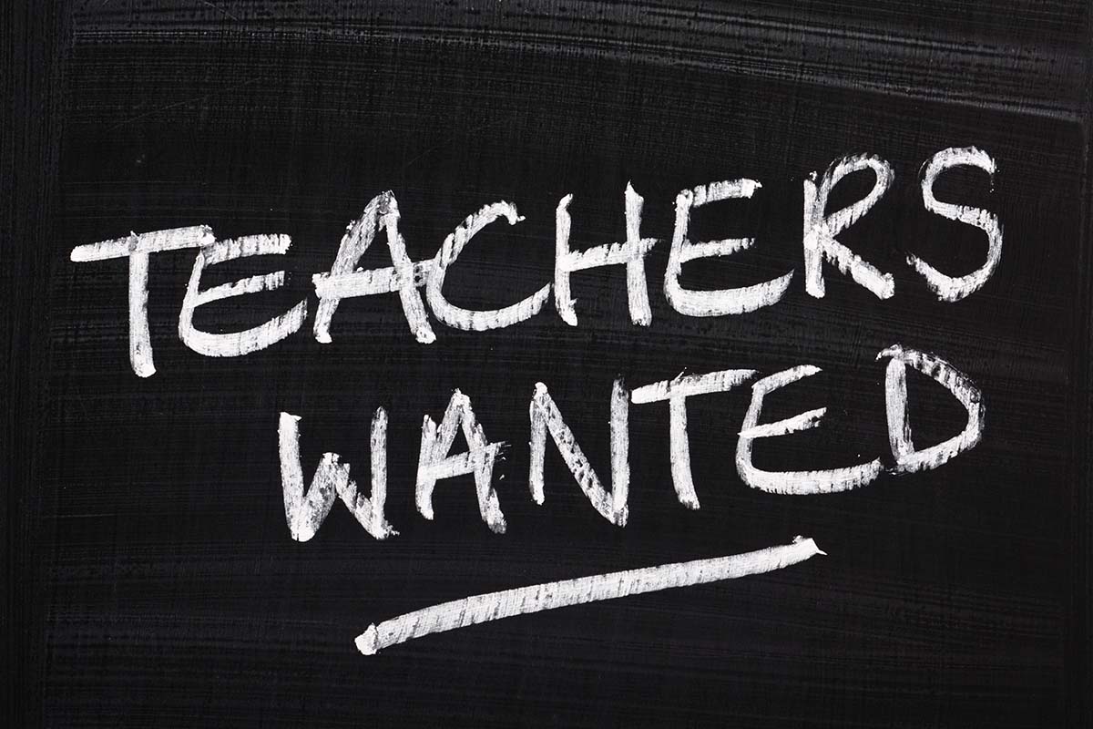 Teachers Wanted written in white chalk on a just wiped blackboard