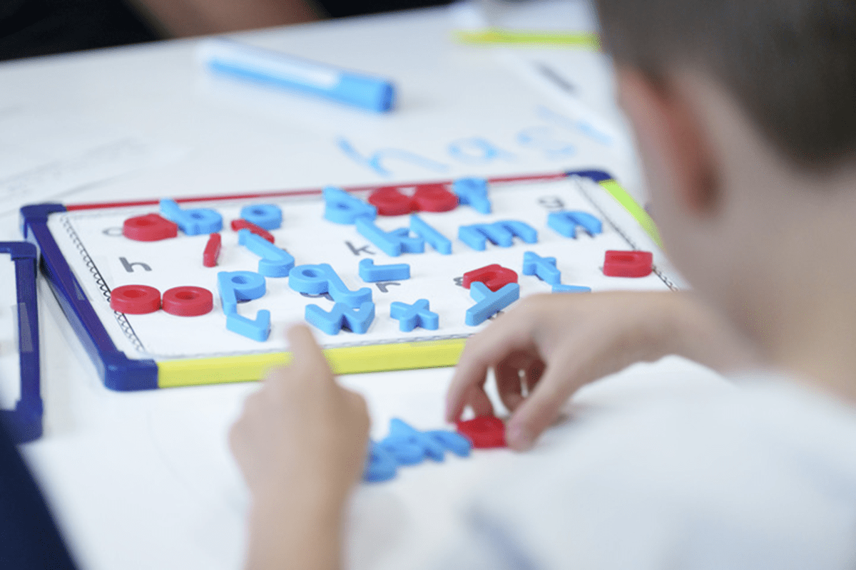 A view of a child from the back.  The student is participating in an activity that focuses on practicing letters. 