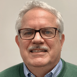 Headshot of a bespectacled man in a blue shirt and green sweater