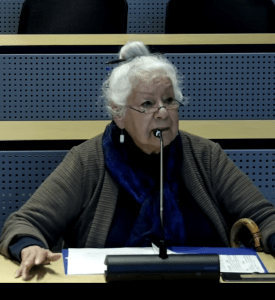 A woman sits in front of a mic addressing a meeting